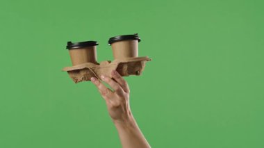 Yeşil krom anahtar arka planına karşı bardak altlığında iki kağıt kahve bardağı tutan bir kadın. Paket servis, kahve kültürü, ofis, iş ve eğitim konuları için ideal.