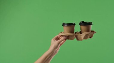 Yeşil krom anahtar arka planına karşı bardak altlığında iki kağıt kahve bardağı tutan bir kadın. Paket servis, kahve kültürü, ofis, iş ve eğitim konuları için ideal.