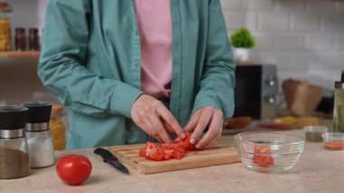 Bir kadın modern bir mutfaktaki bir kaseye taze domates dilimleri koyar. Salata hazırlamak, sağlıklı bir kahvaltı hazırlamak ya da evdeki mutfakta atıştırmak..