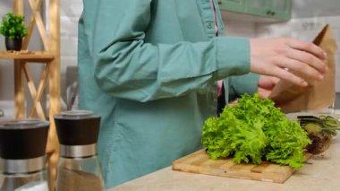 Bir kadın, modern bir mutfakta salata hazırlıyor. Taze sebzeler ve mutfak gereçleri görünür..