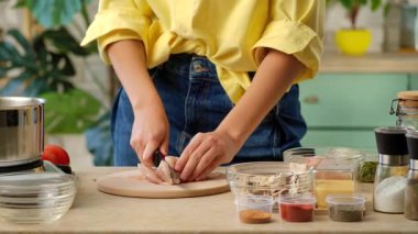 Baharat ve sebzelerle çevrili bir kesme tahtasıyla çiğ tavuk göğsü kesen bir kadının yakın plan fotoğrafı. Ev mutfağında öğle veya akşam yemeği hazırlıyorum..