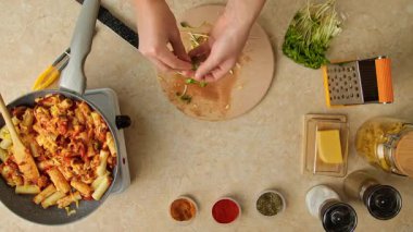 Bir kadının tavuklu, mantarlı, domatesli ve sebzeli makarna yaptığı mutfak masasının üst görüntüsü. Sıcak bir ev mutfağında öğle ya da akşam yemeği için makarna hazırlıyorum..