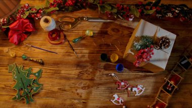 Noel hediye paketleme sahnesinin üst görüntüsü. Kurdeleler, makas, boya ve kır ağacından yapılmış masa üzerindeki ev yapımı dekorasyonlar. DIY tatil hazırlıkları için metin için alanı olan şenlikli arkaplan.