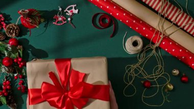 Noel hediyelerini el sanatları kağıdına sarıp yeşil arka planda kırmızı bir fiyonkla bağlayan iki insanın Noel atmosferini ve tatilin sıcaklığını sembolize eden en iyi görüntüsü..