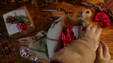 Noel Baba 'nın, Noel' in gelişini ve Noel hazırlıklarını sembolize eden, kartlar, boyalar ve çelenkler arasında tahta bir masanın üzerinde çantasına hediyeler katlayan eldivenli ellerinin üst görüntüsü..