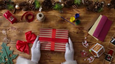 Noel Baba 'nın eldivenli elleriyle kırsal bir masada kendi elleriyle hediyeler yaratması. Yılbaşı ve Noel kutlamalarına hazırlanılıyor.