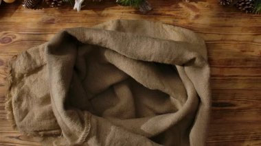 Noel Baba 'nın, Noel' in gelişini ve Noel hazırlıklarını sembolize eden, kartlar, boyalar ve çelenkler arasında tahta bir masanın üzerinde çantasına hediyeler katlayan eldivenli ellerinin üst görüntüsü..