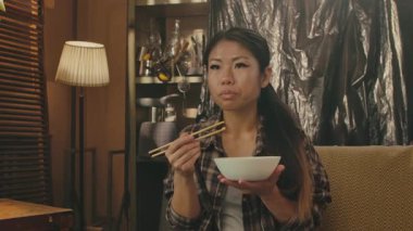 A Korean woman savoring traditional Asian food with chopsticks in a cozy home setting.