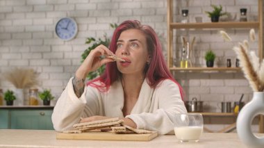 Kızıl saçlı bir kadın şık bir mutfak ortamında gevşemiş bir ruh hali yayarak taze ekmekten hoşlanır. Ev mutfağında kahvaltı, yemek yeme ritüeli..