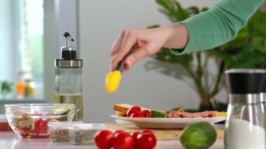 Yeşil kazaklı bir kadın kahvaltı hazırlar ve domatesleri kızarmış sosis, pastırma ve mantarla birlikte tabağa koyar. Etrafında çeşitli malzemeler var. Ev mutfağında yemek hazırlamak..