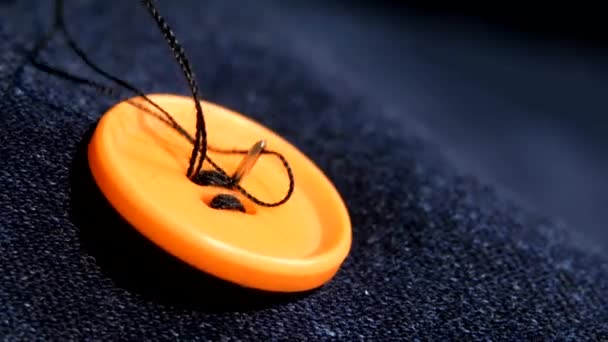Coser un botón naranja en jeans, mezclilla, de cerca — Vídeos de Stock