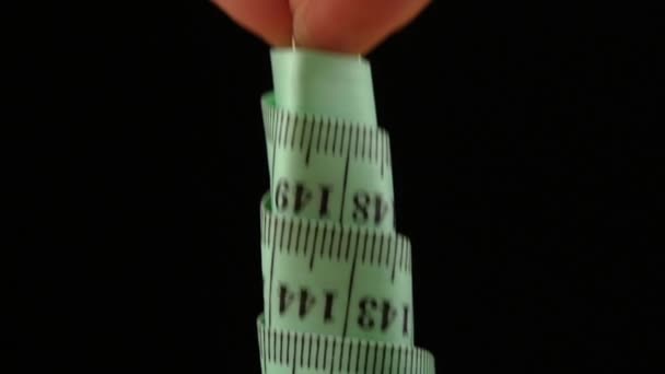 Hand losmaken van een spoel van Turquoise meetlint op zwarte achtergrond, close-up, Slow Motion — Stockvideo
