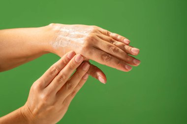 Canlı yeşil bir arka planda cilde nemlendirici krem sürerken elinizi kapatın. Güzellik konsepti, cilt bakımı ve krem ürün sunumu.