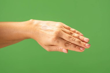 Canlı yeşil arka plana nemlendirici sürerken, pürüzsüz cilt bakımı sergilenen bir eli kapat. Güzellik konsepti, cilt bakımı ve krem ürün sunumu.