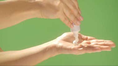 Parlak yeşil bir arka planda, tüpten nemlendirici krem sıkarak ellerini kapat. Güzellik konsepti, cilt bakımı ve krem ürün sunumu.