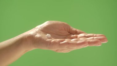 Üzerine nemlendirici krem damlayan bir kadın avucunun kapağı, yeşil krom anahtar arka plan. Güzellik, cilt bakımı ve krem sunumu kavramı.