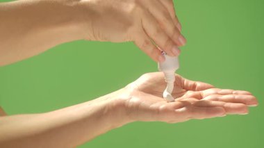 Parlak yeşil bir arka planda, tüpten nemlendirici krem sıkarak ellerini kapat. Güzellik konsepti, cilt bakımı ve krem ürün sunumu.