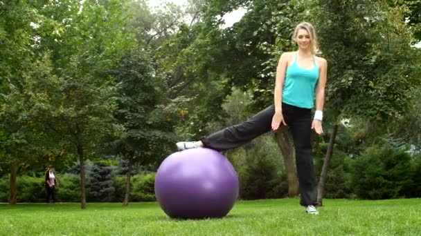 Jonge vrouw zitten op touw met een bal in het park — Stockvideo