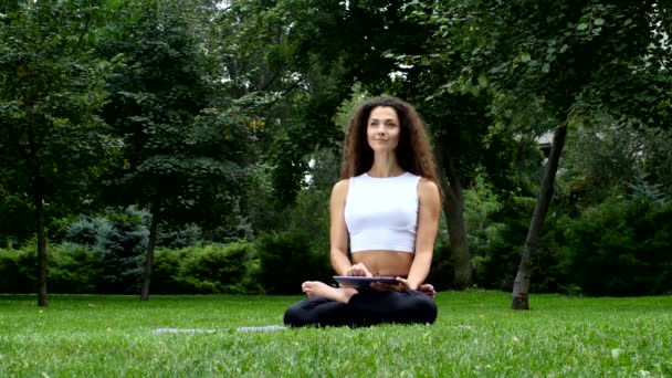 Mujer joven yoga en el parque trabajando en una tableta pc — Vídeo de stock