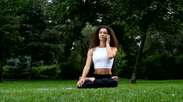 Молода жінка йога в парку розмовляє по телефону — стокове відео