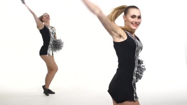 Две девушки танцуют с помпонами в руках. белый фон, замедленное движение — стоковое видео