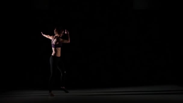 Unusual contemporary moves making by girl in the shadow on black background, slow motion