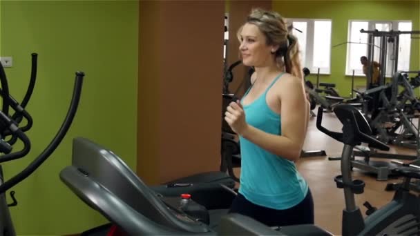 Atletisk flicka klädd i blå t-shirrt gör en övning på löparbana i gymmet — Stockvideo