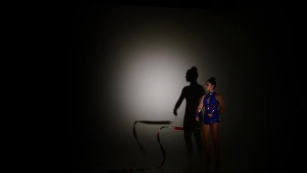 Girl gymnast with color ribbon on black background, slow motion — Stock Video