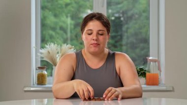 Mutfakta oturmuş kuru üzüm yiyen bir kadın. Tombul bir kadın yaz sabahı sağlıklı bir vejetaryen kahvaltısının tadını çıkarır..