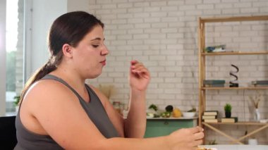 Modern bir mutfak ortamında kahvaltıdan zevk alan bir kadın dikkatli bir yemek ve rahatlama anı yakalıyor..