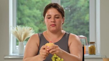 Bir kadın pencerenin kenarında oturur, düşünceli bir şekilde bir dilim şeftalinin tadını çıkarırken yeşilliğe bakar..