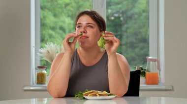 Bir kadın masada oturmuş taze salata yapraklarının tadını çıkarıyor, rahat bir evde sağlıklı bir yaşam tarzı sergiliyor..