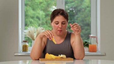 Bir kadın mutfak masasında oturmuş kahvaltısının tadını çıkarıyor tatlı olarak sulu olgun kavun dilimleri yiyor. Sağlıklı, çevre dostu bir vejetaryen kahvaltısı..