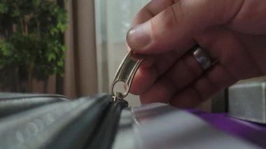 Parlak bir odada plastik fermuar ve metal tokayla valizi bağlayan bir elin makro görüntüsü..