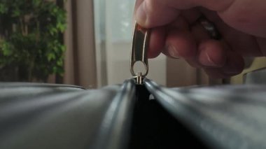 Parlak bir odada plastik fermuar ve metal tokayla valizi bağlayan bir elin makro görüntüsü..