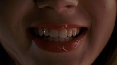 Bir kadının yüzünün alt kısmının detaylı bir yakın çekimi, onun gülümseyen, parlak kırmızı dudaklarına odaklanmak, rujunun dokusunu ve parlaklığını vurgulamak,.