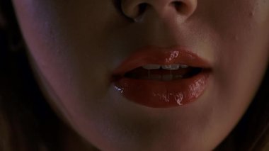 Bir kadının yüzünün alt kısmının detaylı bir yakın çekimi, parlak dudaklarına odaklanmış, rujunun dokusunu ve parlaklığını vurguluyor. Kadın seni seviyorum diyor.