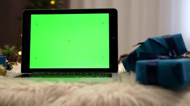 Kabarık bir yüzey üzerinde yeşil ekranı olan bir dizüstü bilgisayar, Noel süsleri ve hediyelerle çevrili..