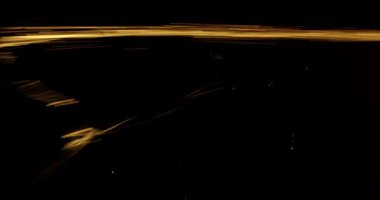 Stüdyonun siyah yalıtımlı arka planına karşı altın ışık huzmelerinde sıvı ağ sıçraması. Sıvı havaya püskürtülür ve ağ parçacıkları düşer. Yavaş çekim.