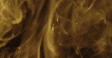 Koyu bir arkaplan üzerinde ışıldayan parçacıklarla zarifçe dönen altın duman. Yavaş çekim.