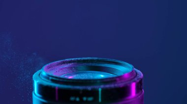 Mavi neon ışıklı bir kamera merceği ve ince toz bulutu sanatsal bir atmosfer yaratıyor..
