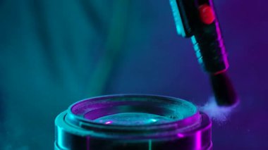 Toz parçacıklarını temizlemek için bir fırçayla temizlenen, parlak neon ışıklarıyla aydınlatılan, toz parçacıklarını gösteren bir kamera merceği. Yavaş çekim.