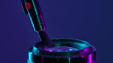 Toz parçacıklarını temizlemek için bir fırçayla temizlenen, parlak neon ışıklarıyla aydınlatılan, toz parçacıklarını gösteren bir kamera merceği. Yavaş çekim.