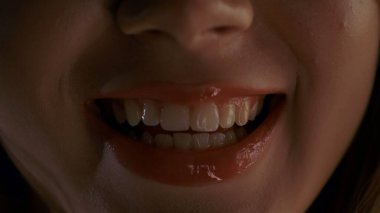 Bir kadının yüzünün alt kısmının detaylı bir yakın çekimi, onun gülümseyen, parlak kırmızı dudaklarına odaklanmak, rujunun dokusunu ve parlaklığını vurgulamak,.