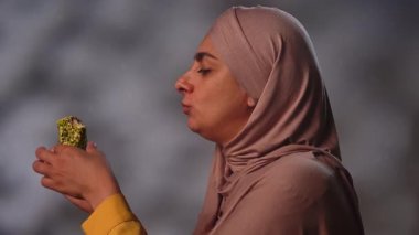 Akşamları tesettürlü Müslüman bir kadının tatlı olarak fıstıklı rakhat lokum yediğini görüyorum. Geleneksel Arap başlığı giyen Doğulu bir kadın..