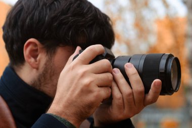 Sonbaharda elinde fotoğraf makinesi olan bir kişi, renkli yapraklarla çevrili bir parkta fotoğraf çekiyor..