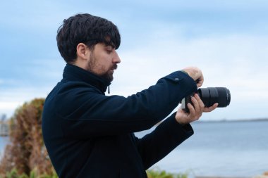Koyu renk ceketli bir adam bulutlu bir gökyüzünün altında kamerayı ayarlıyor..