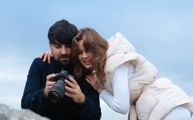 Gülümseyen bir çift, bulutlu bir günde dışarıda dikilirken dijital kamerada fotoğraflara yakından bakar..
