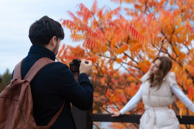 Sırt çantalı bir fotoğrafçı renkli sonbahar yapraklarının önünde poz veren bir kadının fotoğrafını çeker..
