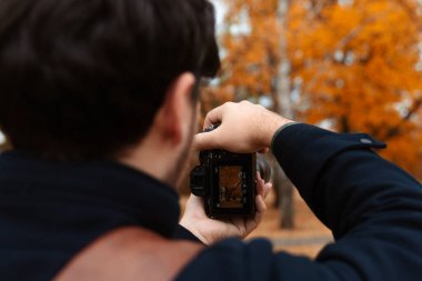 Bir kişi arka planda turuncu yapraklı canlı bir sonbahar sahnesini çekmek için bir kamera tutuyor..